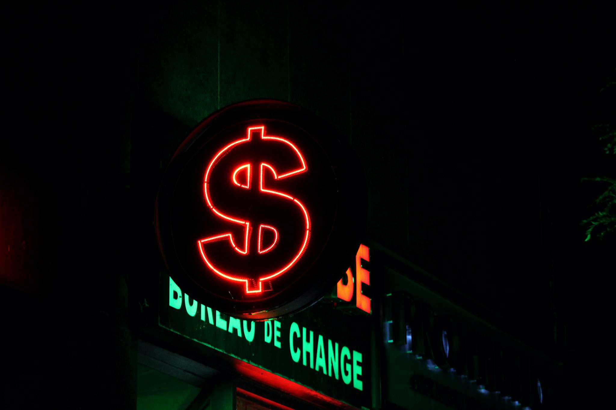 Close-up of a glowing red dollar sign neon at a currency exchange bureau.